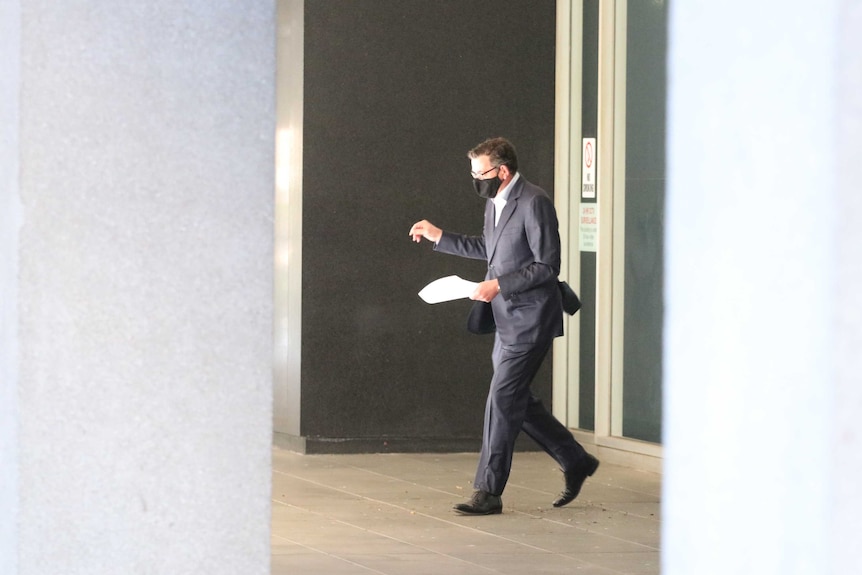 Daniel Andrews walking with a sheet of paper in a suit and mask to a press conference.