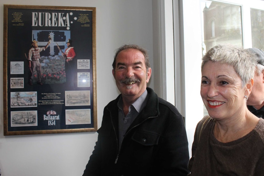 Tony Cooke smiles has he walks with his wife past a eureka poster.