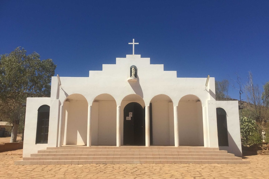 A white church adorned with a cross and figure of the virgin mary sits in regional australia.