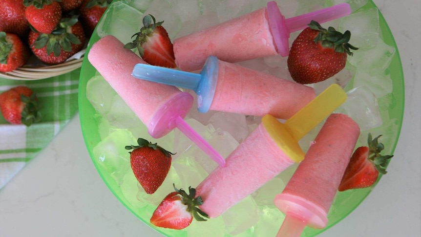 Strawberry frozen yoghurt pops on a plate with some whole strawberries