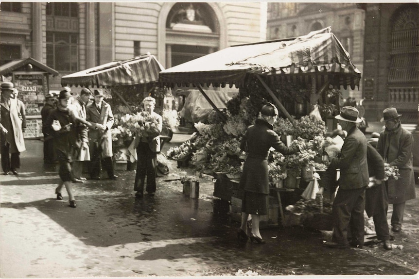 An old photo of a man holding flowers, people bustling around