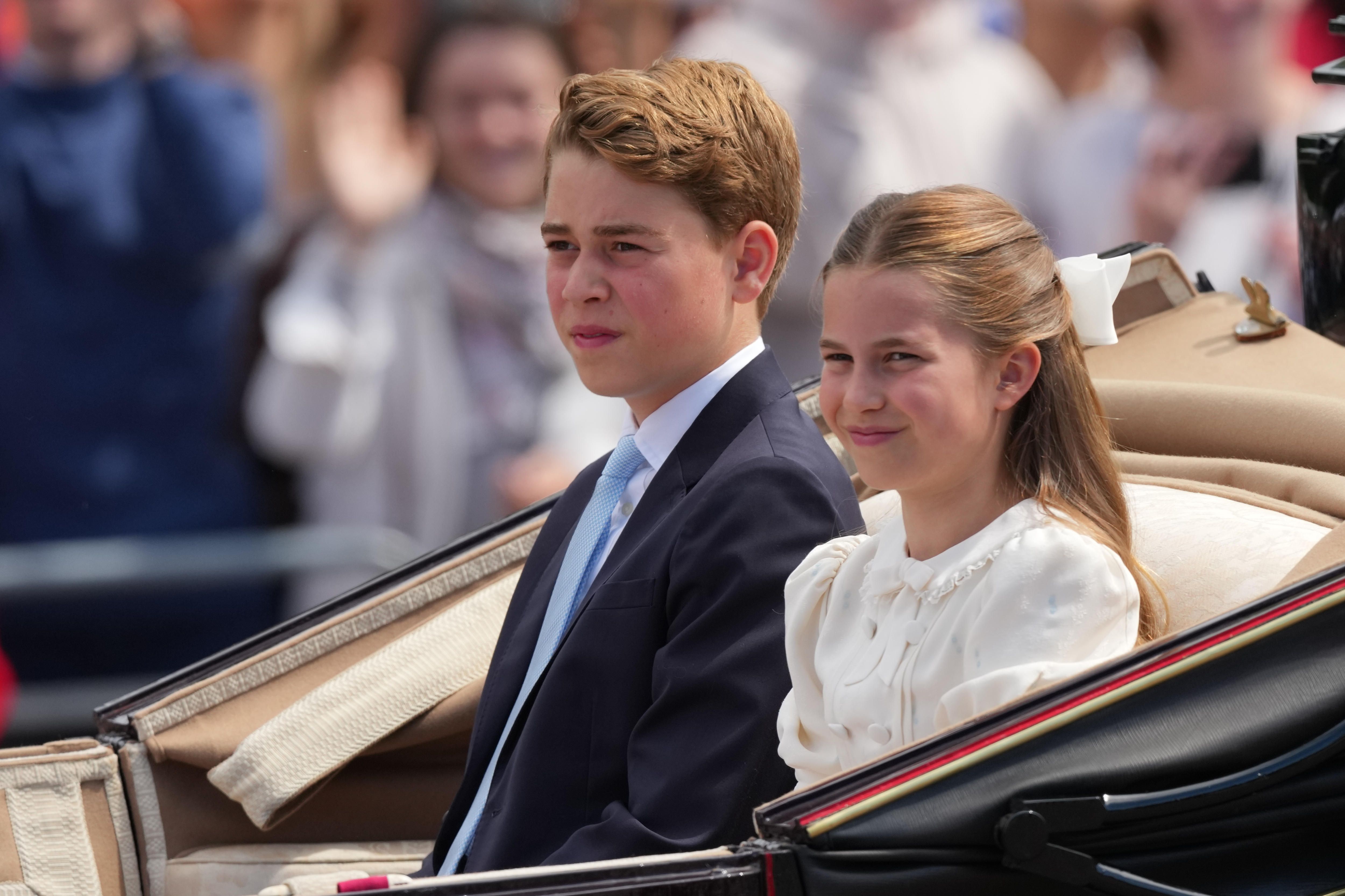 A boy and a girl in formal dress sit in a carriage as crowds look on.