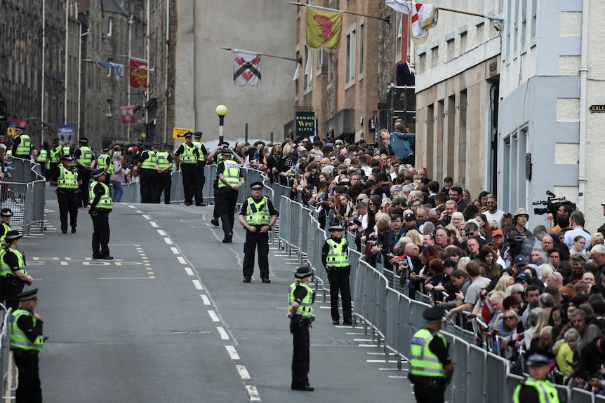 Crowds stand against barricades as police in hi-vis watch the route. 