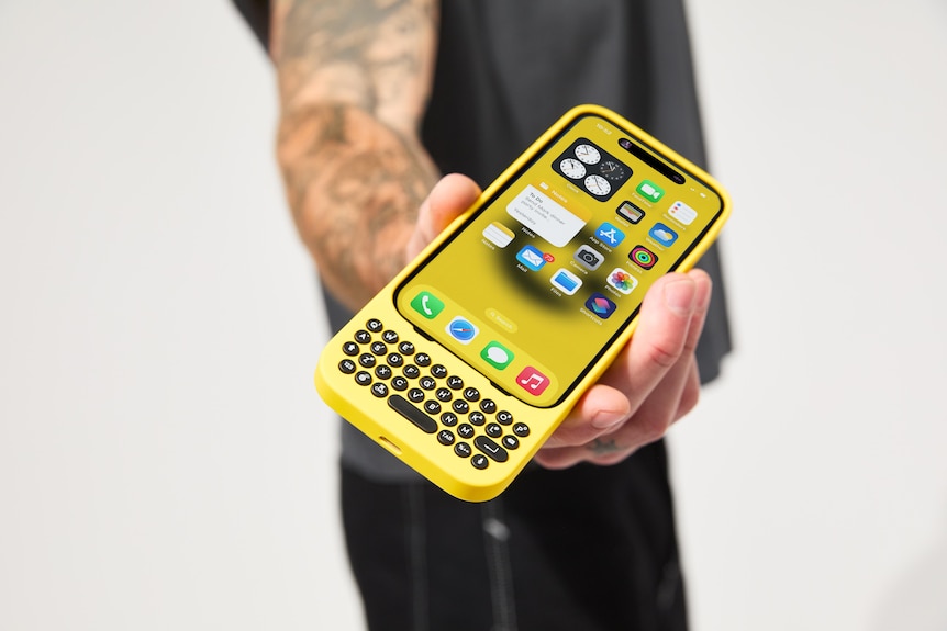 A close up of a man's hand holding out an iPhone in a case which puts a small physical QWERTY keyboard below the device's port.