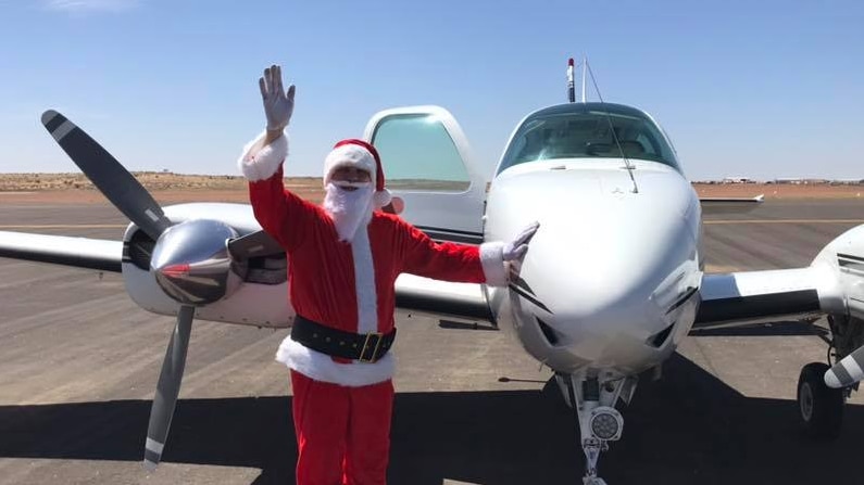 Ken Skelly dressed as santa waving in Birdsville in front of his plane