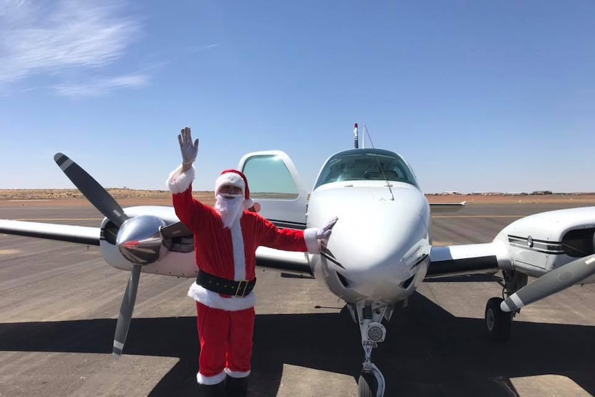 Ken Skelly dressed as santa waving in Birdsville in front of his plane