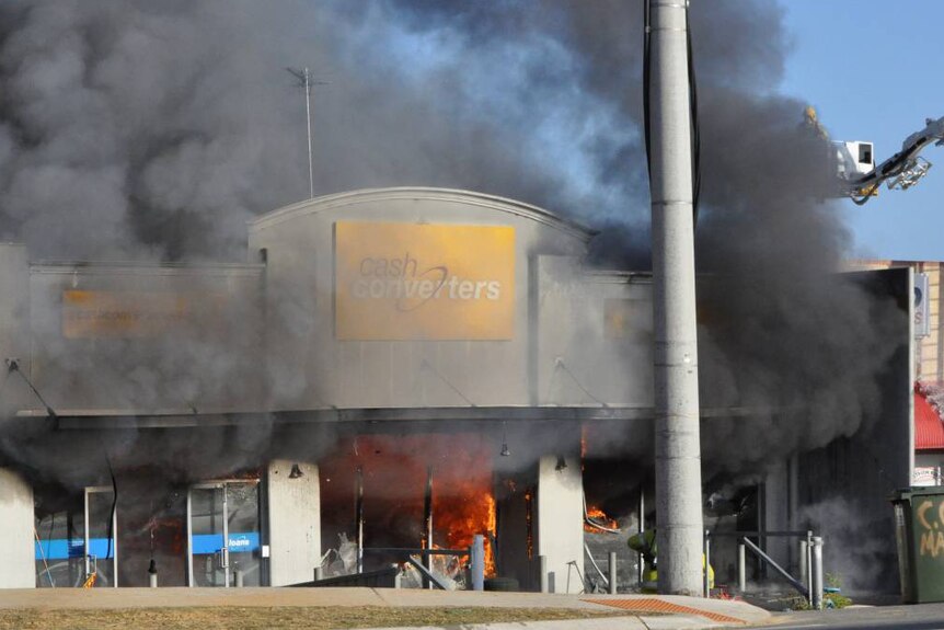 Clouds of black smoke billow from a burning Cash Converters store with flames visible inside.
