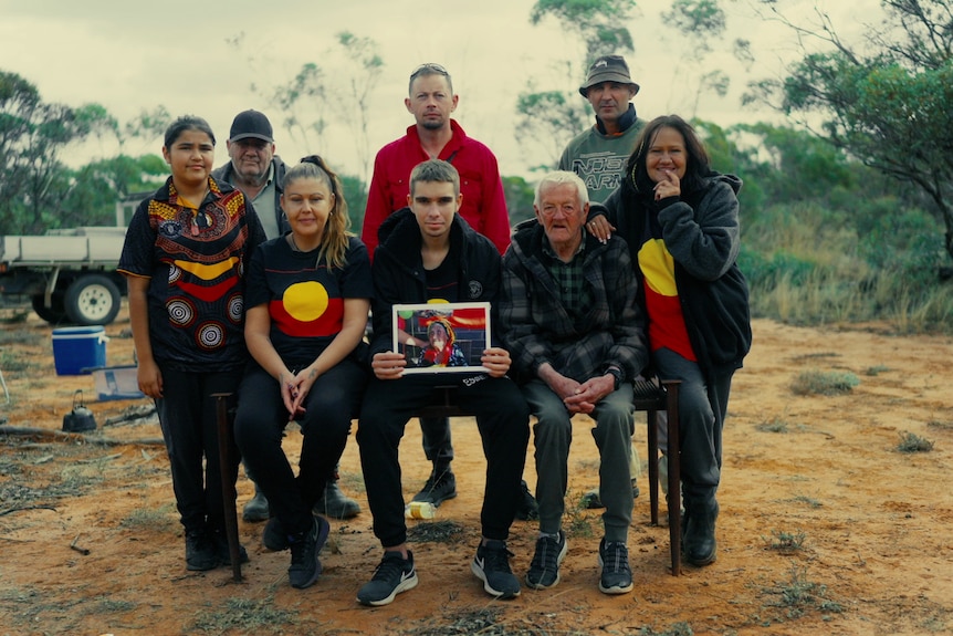 A family of eight gathered in a formal portrait. They are on their country, and look proud.