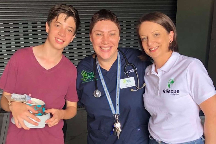 Three people standing together holding dog food bowls.