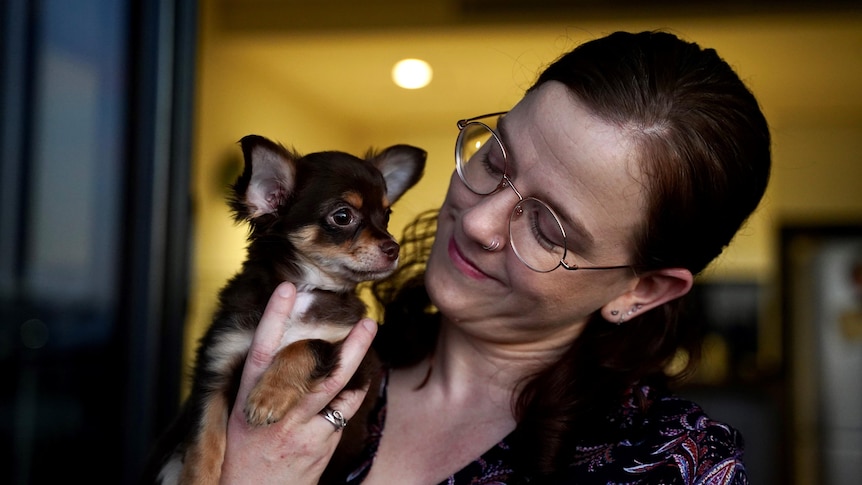 woman looks lovingly at her chihuahua puppy who fits in her hand