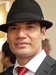 A man in a jacket, dinner shirt and red tie wearing a hat