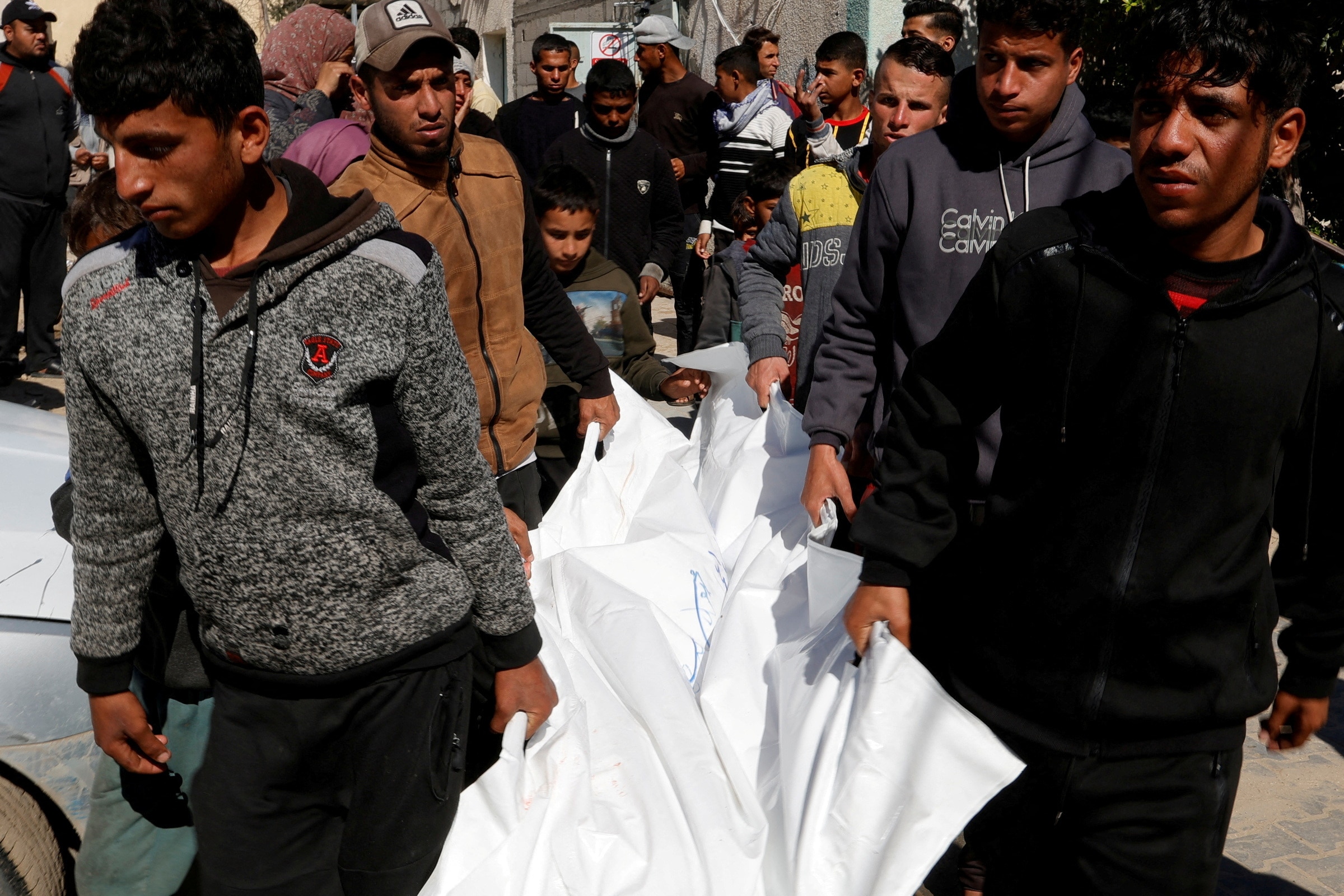 Young men carry a body that has been wrapped in a white sheet through a street outside