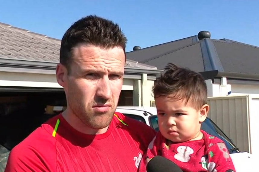 Headshot of a man carrying his infant son, both wearing red.