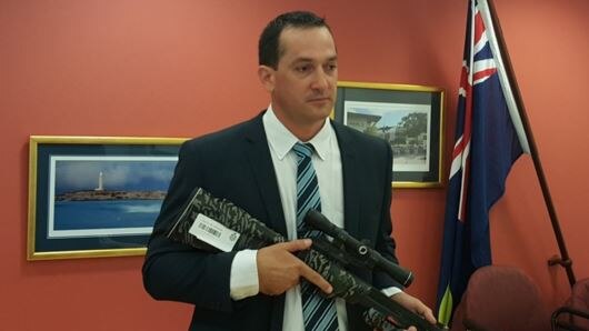 A detective holds a stolen gun seized in raids in WA.