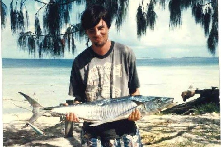 Young man standing on beach holding a large silver fish.