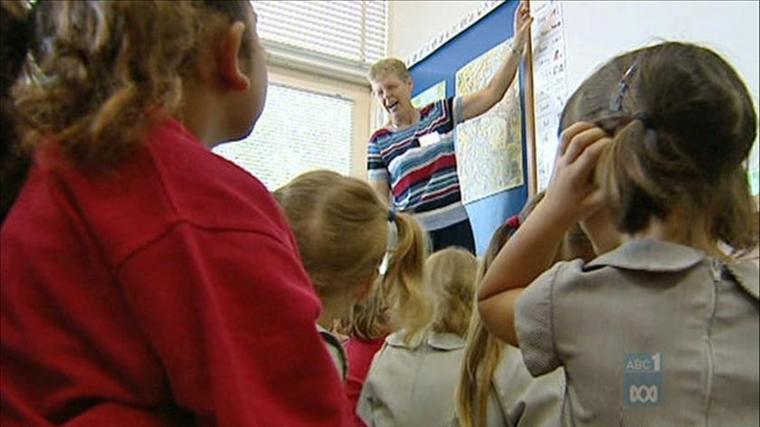 A teacher points to the board in front of primary school students