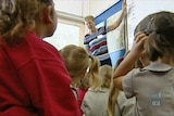 A teacher points to the board in front of primary school students