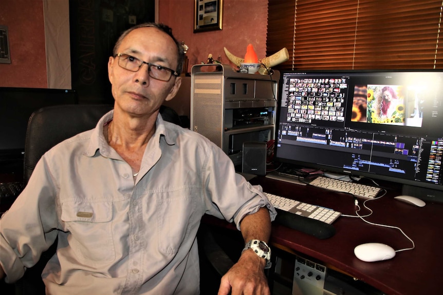 A man stares at the camera with a computer editing suite in the background.
