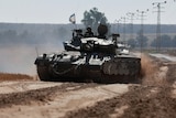 A soldier mans a gun atop a tank that flies the Israeli flag in the desert