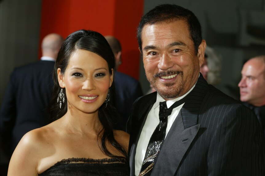 A man in a black suit next to a woman in a black dress on the red carpet.