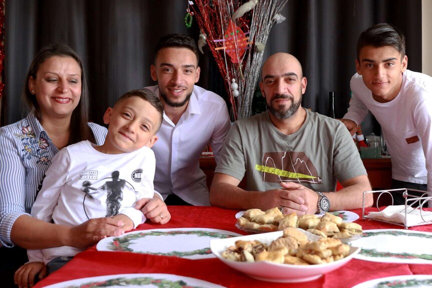 a Family of five pose at a table decorated with a Christmas tablecloth and other decorations
