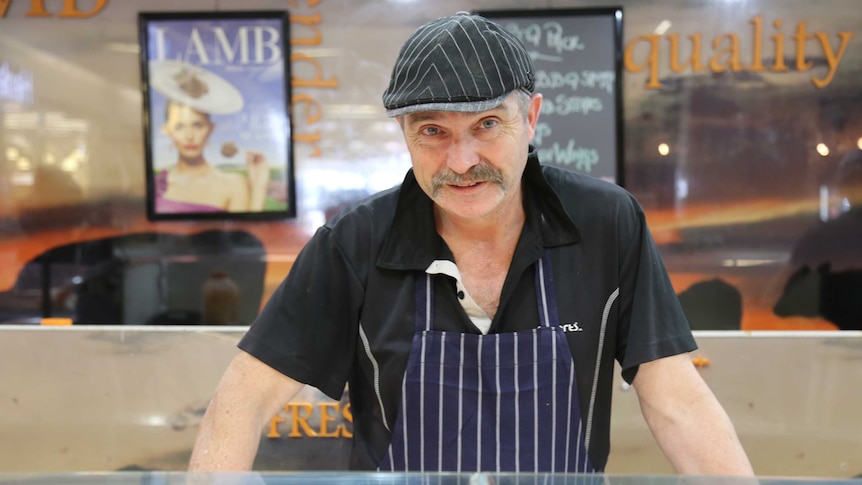 A butcher looks at the camera while standing above his selection of meat