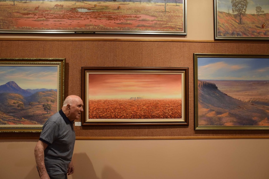 Old man on left hand side of screen walking to the right with vivid landscape paintings in the background