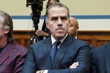 A close-up of Hunter Biden, sitting between people in a Committee room, wearing a suit and tie and crossing his arms.