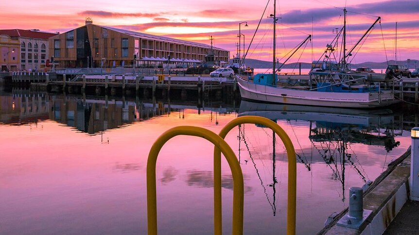 Boats and a jetty are lit up by a sunrise in Hobart.