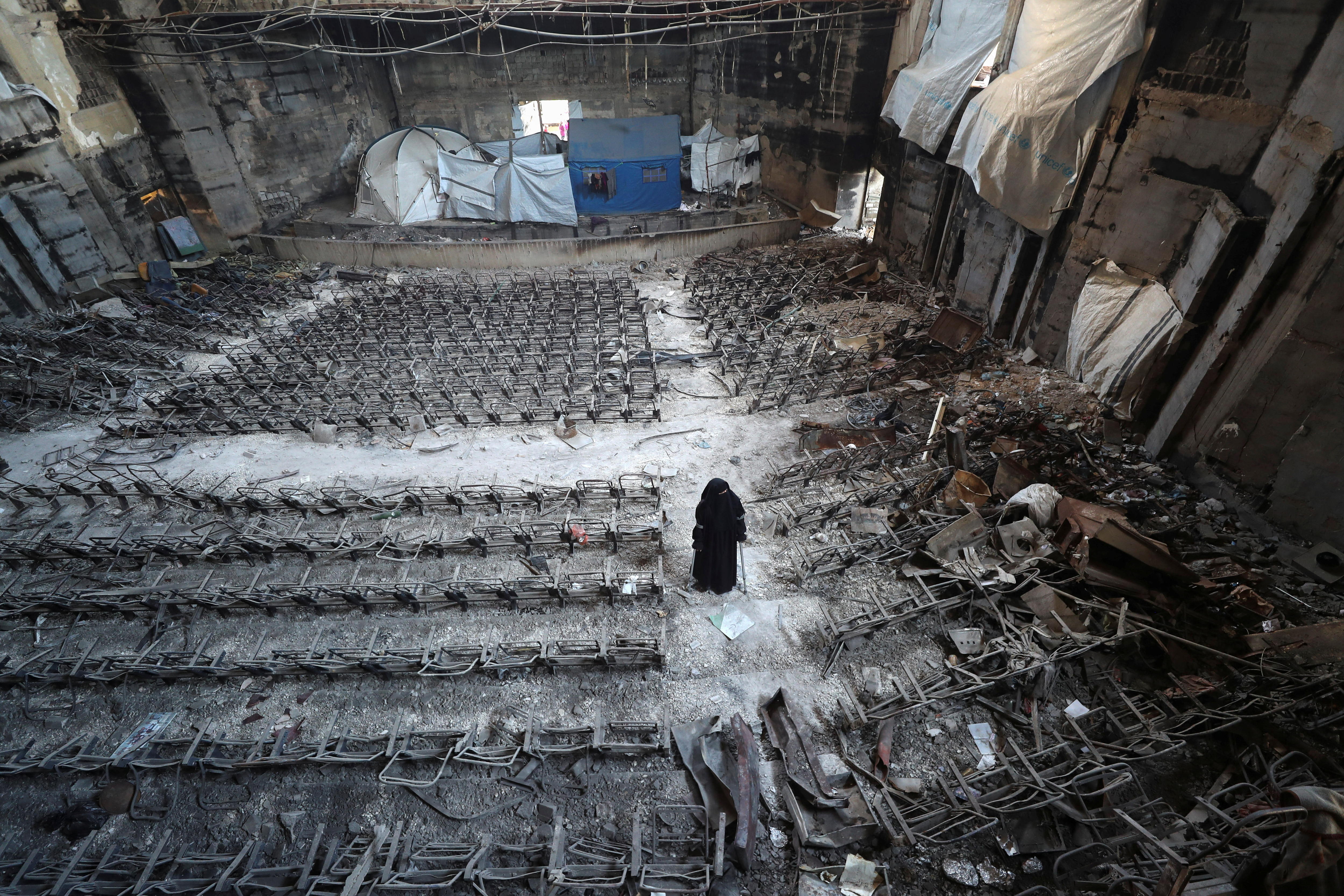 An aerial shot of a destroyed auditorium, seats are blacked and crumpled with a few tents set up.