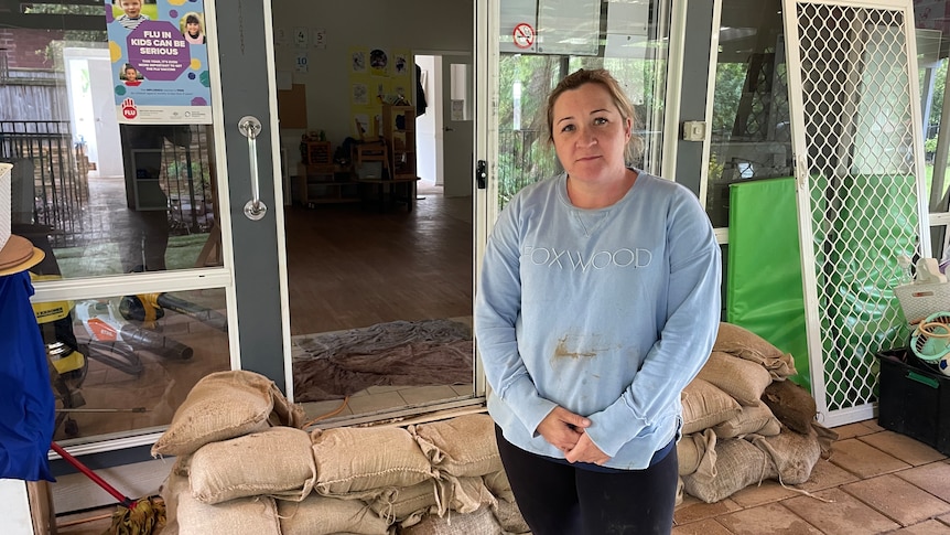 Woman in blue jumper stands in front of sandbags piled up in front of a door