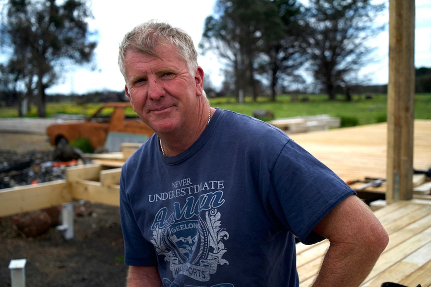 Jonny Gloyne, wearing a blue shirt, with a half-built verandah behind him.