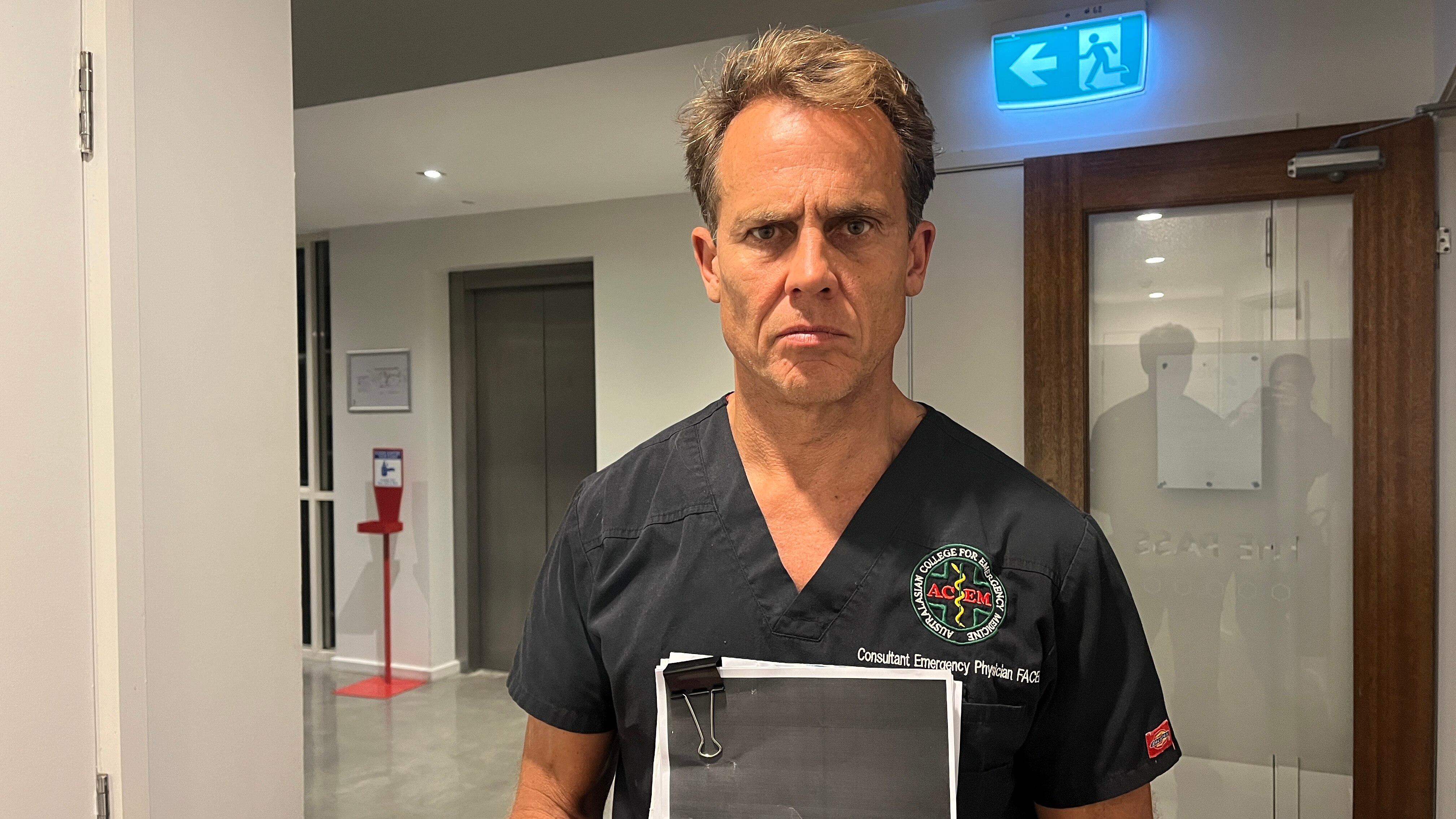 Un hombre con matorrales negros se encuentra en un vestíbulo, luciendo serio y preocupado.