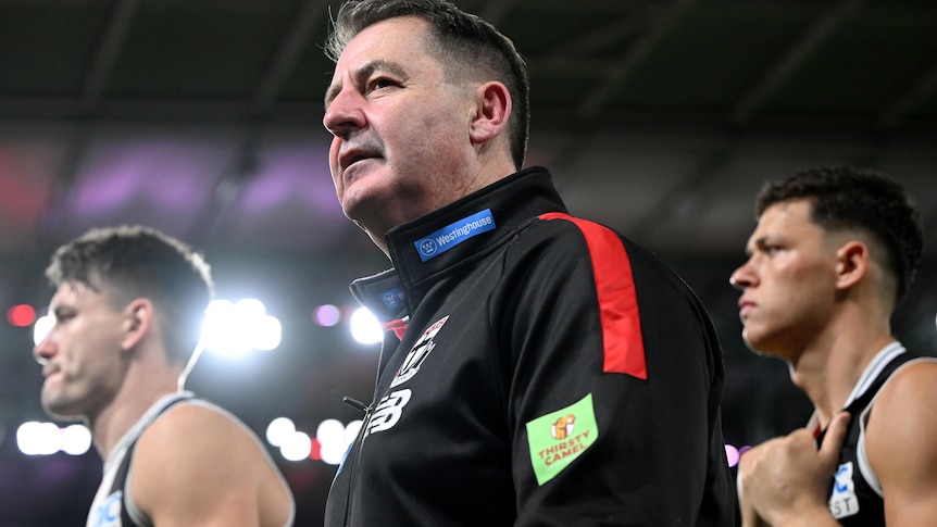 AFL coach Ross Lyon walking off the ground with two players after a match