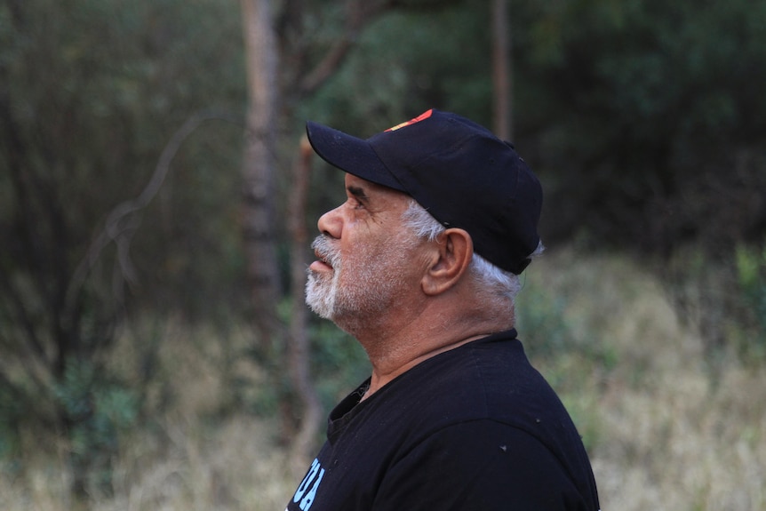 Indigenous man wearing a black shirt and cap looking up at Uluru.