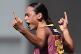 A Brisbane Lions AFLW player raises her arms as she celebrates a goal.