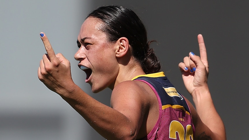 A Brisbane Lions AFLW player raises her arms as she celebrates a goal.