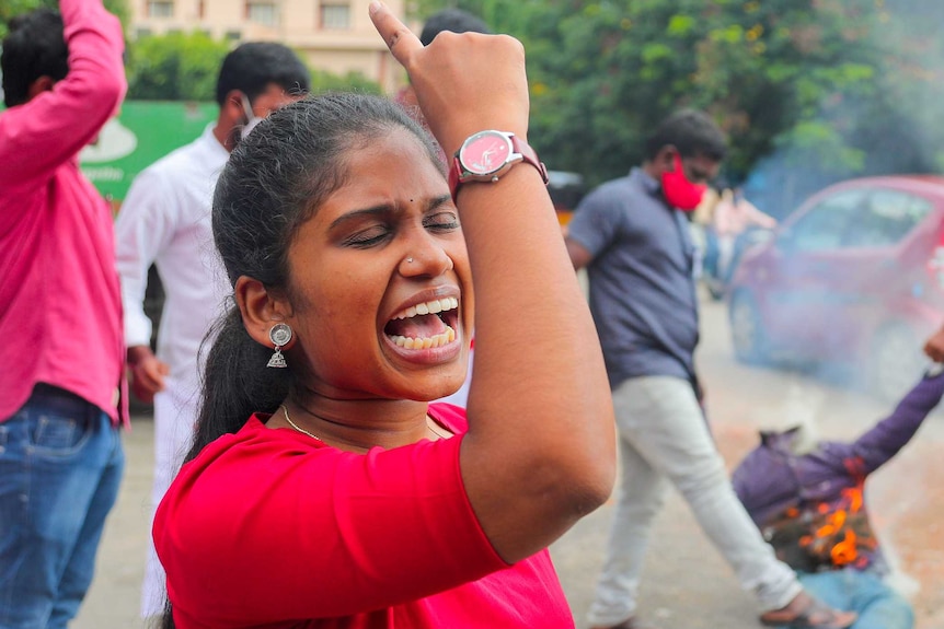 A woman shouting while men burn an effigy behind her