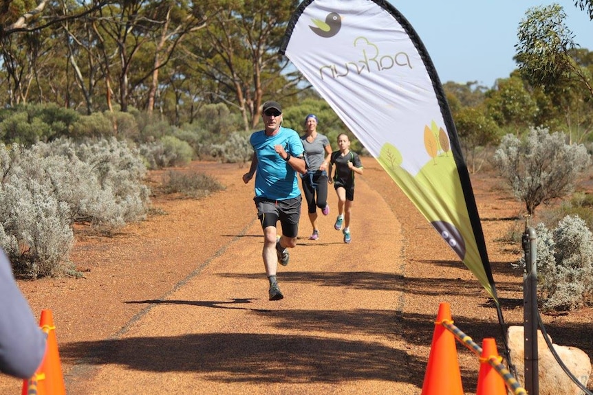 Three people run along a path with trees around them