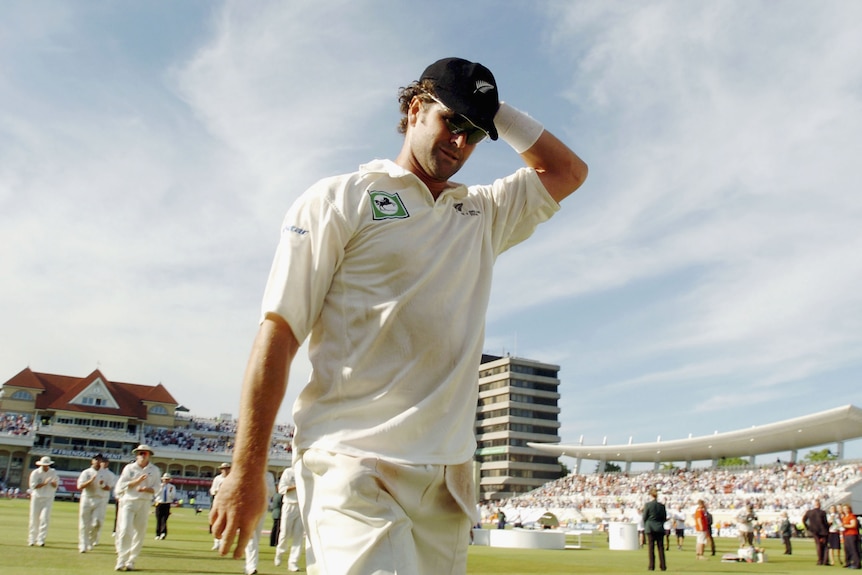 Chris Cairns holds his had and walks off a cricket field