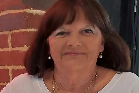 A tight head shot of an older woman with dark hair smiling for a photo.
