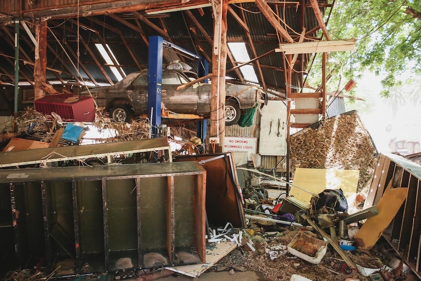 damaged mechanics garage filled with muddy debris, a car up on racks