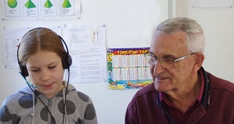 A student wearing headphones is coached by a Volunteers for Isolated Students' Education (VISE) teacher.