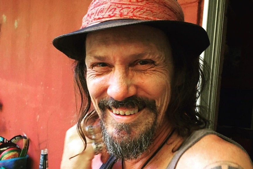 A man wearing a hat smiles at the camera