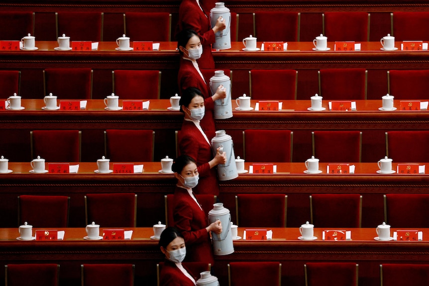 Four women in tiered stairs wearing masks and holding urns of tea.