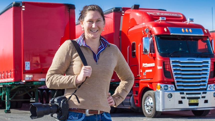 A woman, with a camera over her shoulder, stands in front of a big red truck