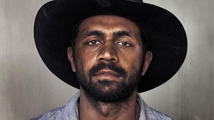 A portrait of an Aboriginal man with a short beard and a black wide-brimmed hat