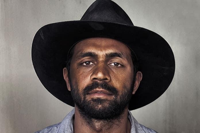 A portrait of an Aboriginal man with a short beard and a black wide-brimmed hat