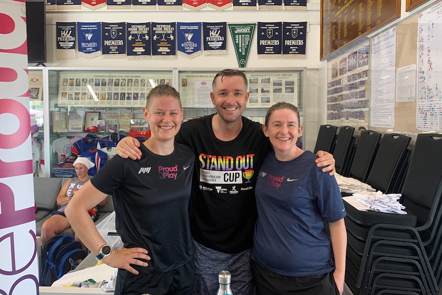 Lauren Foote, Dr Ryan Storr and Christine Granger pose for a photo in front of leader boards in a clubhouse.