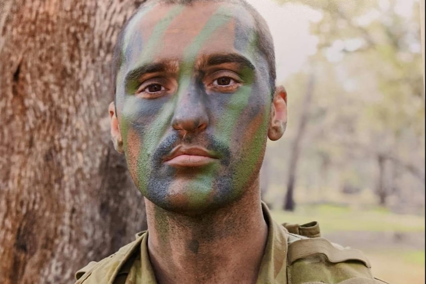 Soldier Brendon Payne wearing camouflage face paint and full gear.